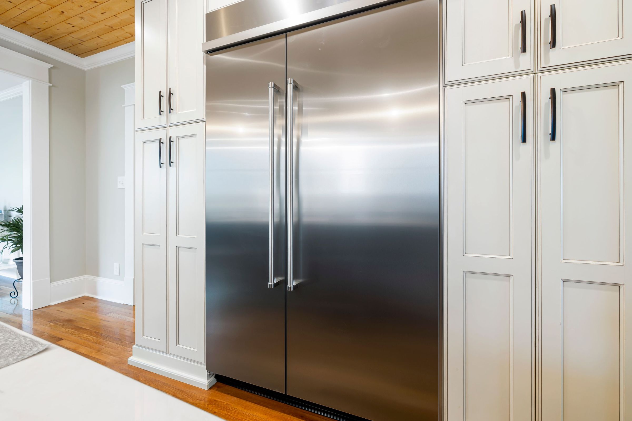 Built-in stainless steel refrigerator between white kitchen cabinets